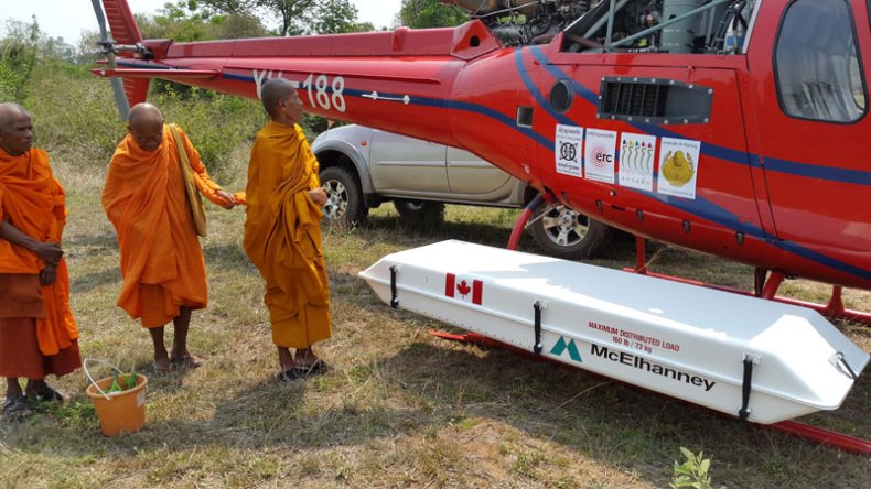 Buddhist monks preparing for a traditional blessing ceremony next to the helicopter and lidar instrument within its pod, at the remote temple complex of Banteay Chhmar.