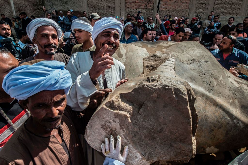 Egyptian workers pose next to an excavated statue, recently discovered by a team of German-Egyptian archeologists, in Cairo's Mattarya district on March 13, 2017.