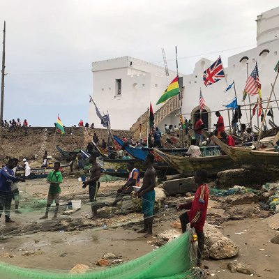 Fishermen in front of Cape Coast Castle, Ghana, with a staircase on the left leading up to a ‘Door of No Return’.