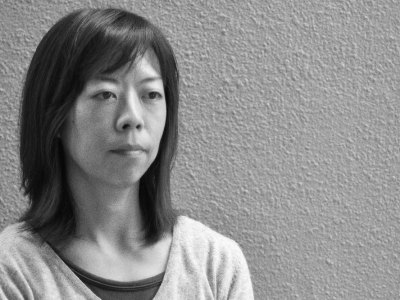 black and white photograph of a Japanese woman standing against a textured wall