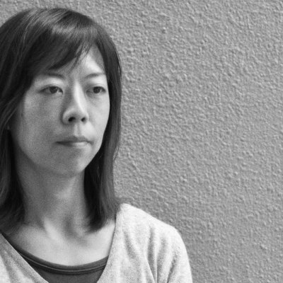 black and white photograph of a Japanese woman standing against a textured wall